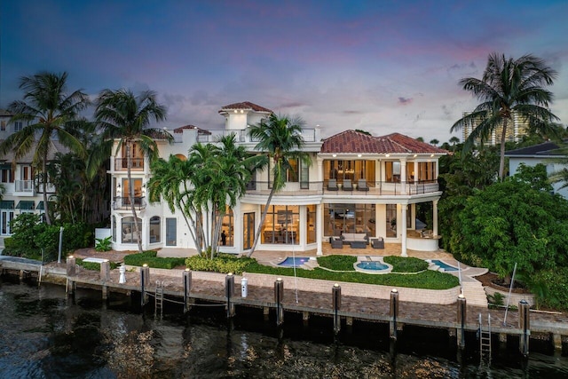 back house at dusk with an outdoor hangout area, a water view, a patio area, and a balcony