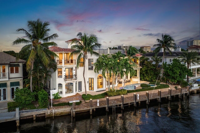 back house at dusk featuring a patio area, a water view, and a balcony