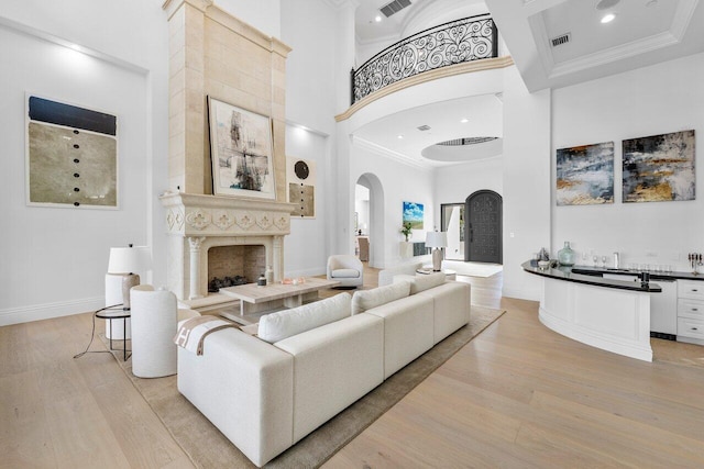 living room with crown molding, a fireplace, a towering ceiling, and light wood-type flooring