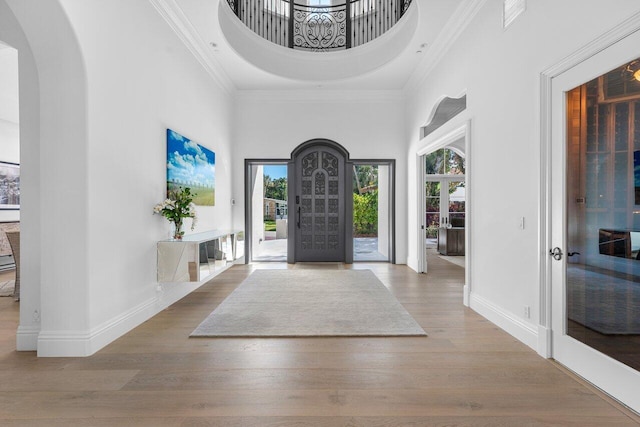 entrance foyer featuring a towering ceiling, ornamental molding, and light hardwood / wood-style flooring