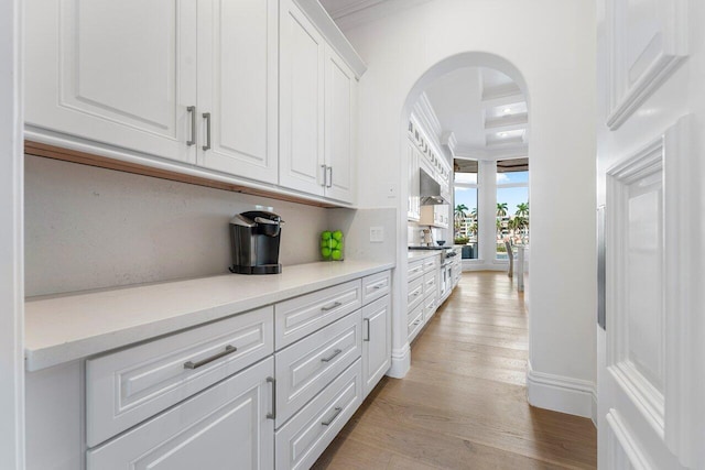 kitchen with light hardwood / wood-style flooring, white cabinets, exhaust hood, and ornamental molding