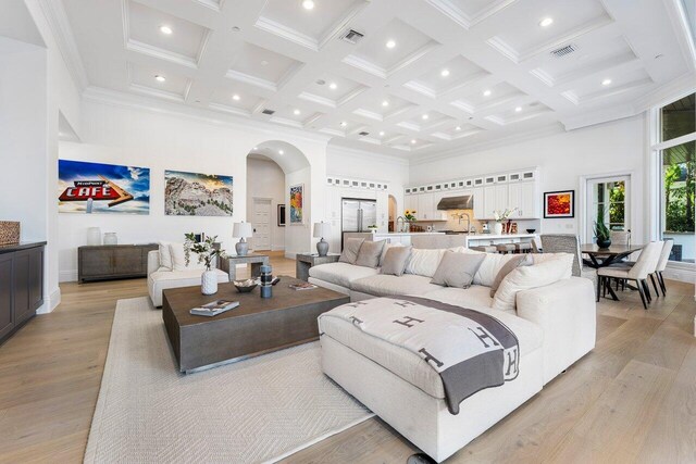 living room featuring beam ceiling, light wood-type flooring, coffered ceiling, and a high ceiling