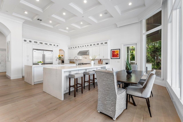 dining room with light wood-type flooring, coffered ceiling, crown molding, beam ceiling, and a high ceiling