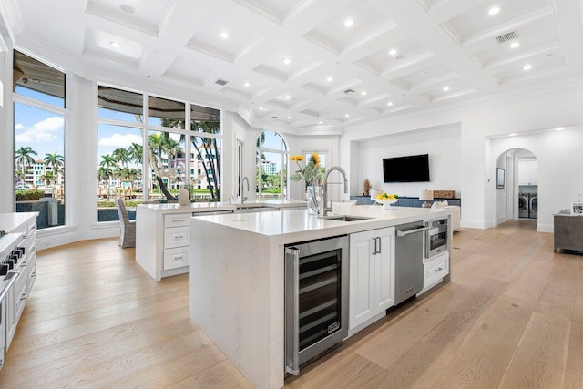 kitchen featuring a kitchen island with sink, white cabinets, sink, a wealth of natural light, and beverage cooler