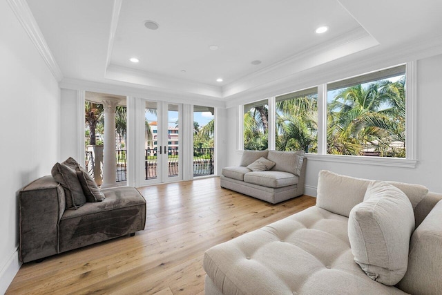 living room featuring french doors, light wood-type flooring, a raised ceiling, and crown molding