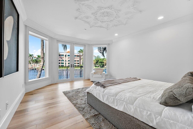 bedroom featuring a water view, light wood-type flooring, crown molding, and access to outside