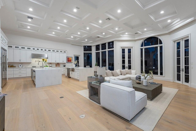 living room with a high ceiling, coffered ceiling, french doors, sink, and light wood-type flooring