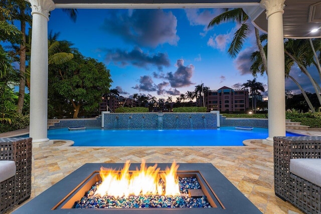 pool at dusk with a patio area, pool water feature, and a fire pit