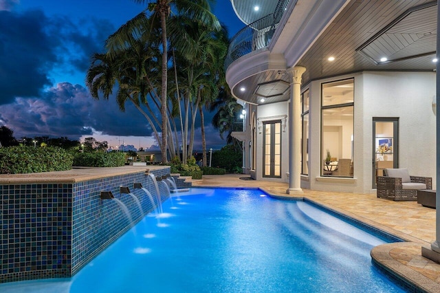 pool at dusk featuring pool water feature and a patio