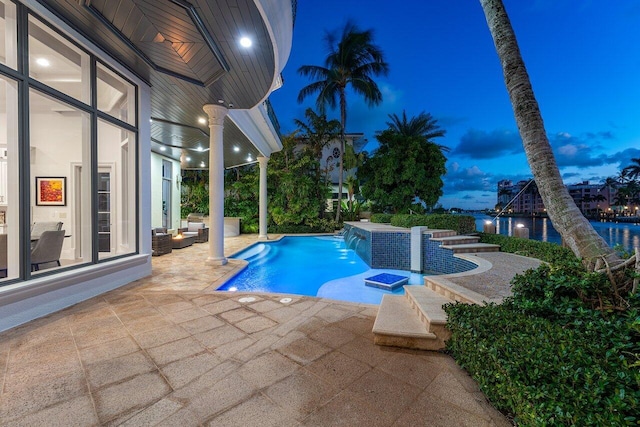 pool at dusk featuring pool water feature, a patio area, a jacuzzi, and a water view