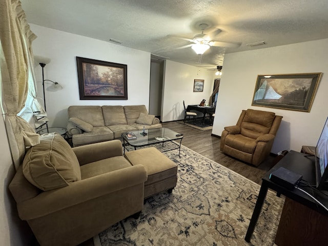 living room featuring ceiling fan, dark wood-type flooring, and a textured ceiling