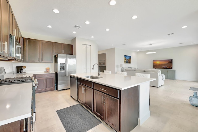 kitchen with dark brown cabinets, light tile patterned flooring, sink, an island with sink, and stainless steel appliances