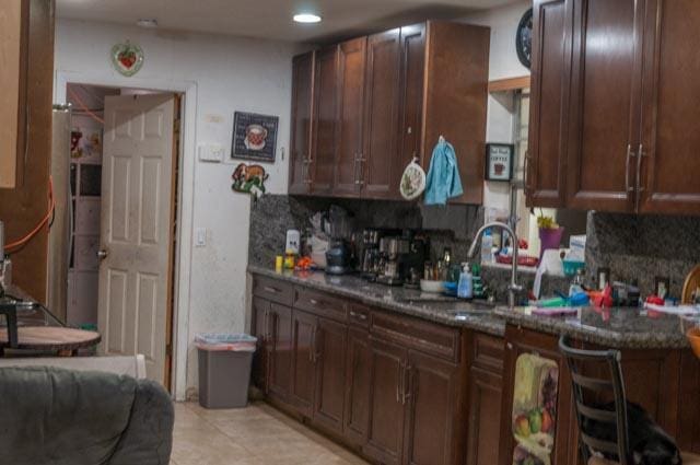 kitchen with dark brown cabinets, backsplash, dark stone countertops, and a sink