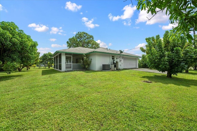 back of property featuring a lawn, a garage, a sunroom, and central AC