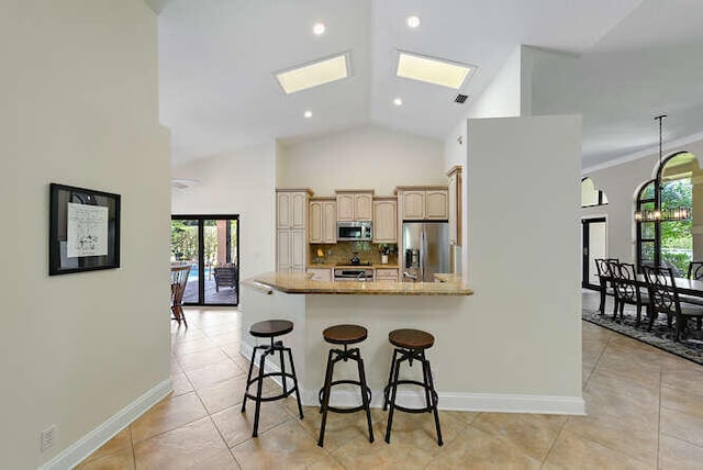 kitchen with light stone counters, a skylight, kitchen peninsula, appliances with stainless steel finishes, and a kitchen breakfast bar