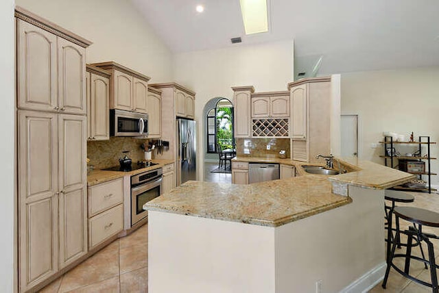 kitchen with vaulted ceiling, kitchen peninsula, a kitchen breakfast bar, stainless steel appliances, and light brown cabinets