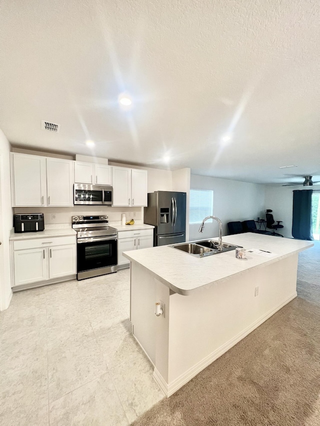 kitchen featuring white cabinets, sink, a center island with sink, appliances with stainless steel finishes, and light colored carpet