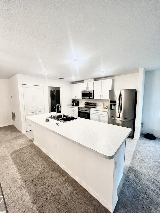 kitchen featuring a kitchen island with sink, light colored carpet, white cabinets, a sink, and stainless steel appliances