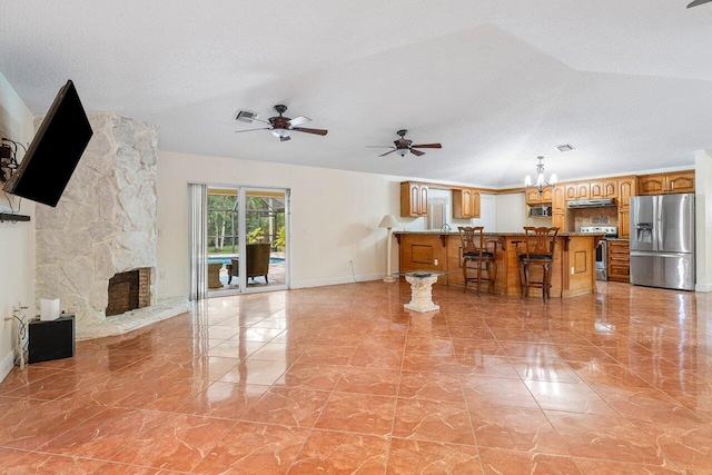 living room featuring a stone fireplace, a textured ceiling, vaulted ceiling, and ceiling fan with notable chandelier