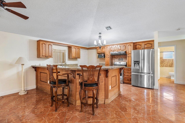 kitchen with light stone countertops, a textured ceiling, kitchen peninsula, a kitchen breakfast bar, and stainless steel appliances