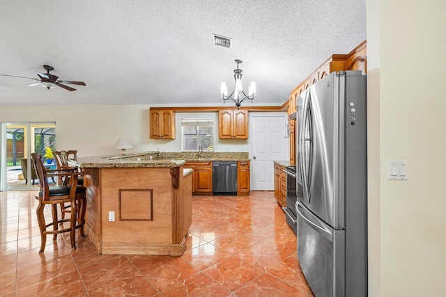 kitchen with a kitchen bar, ceiling fan with notable chandelier, a textured ceiling, stainless steel appliances, and pendant lighting