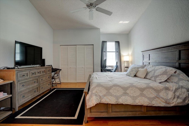 bedroom featuring a closet, a textured ceiling, dark wood-type flooring, vaulted ceiling, and ceiling fan