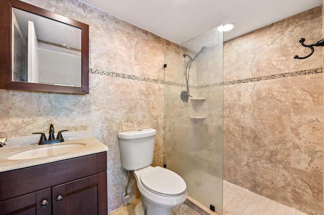 bathroom featuring a tile shower, tile walls, tile patterned floors, vanity, and toilet