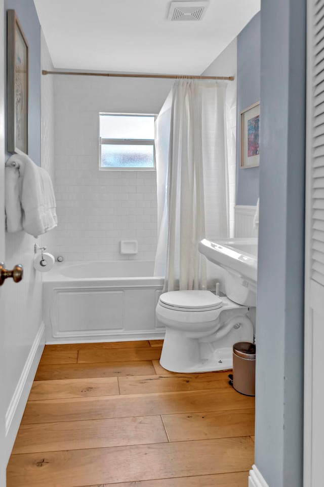 bathroom featuring toilet, shower / bath combination with curtain, and hardwood / wood-style flooring