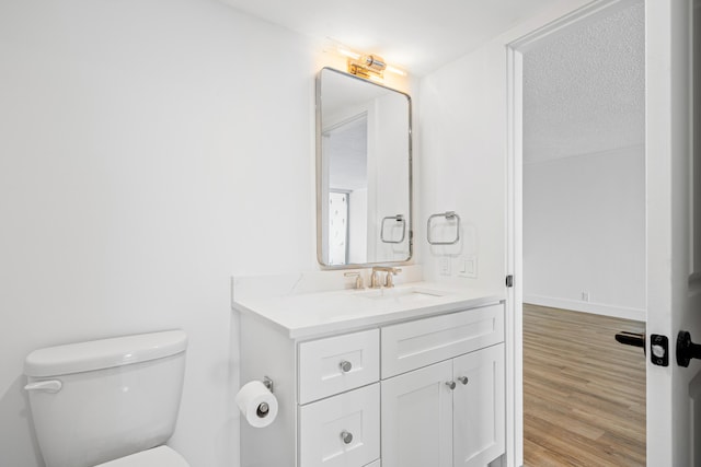 bathroom with wood-type flooring, a textured ceiling, vanity, and toilet