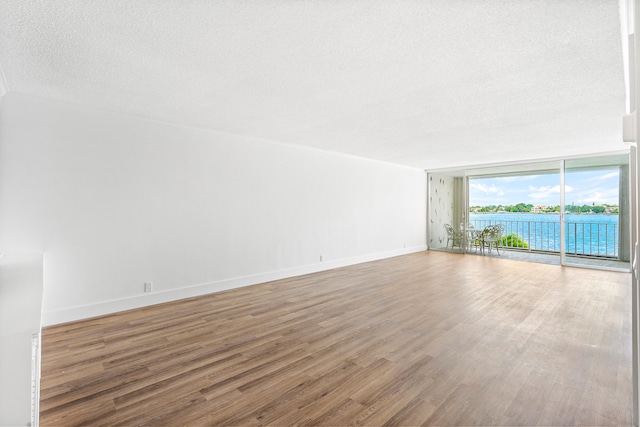 spare room with a textured ceiling, wood-type flooring, a water view, and a wall of windows