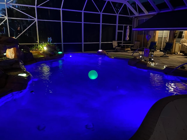 pool at twilight with a patio, pool water feature, and glass enclosure