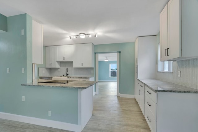 kitchen with light stone countertops, white cabinetry, kitchen peninsula, and light hardwood / wood-style flooring