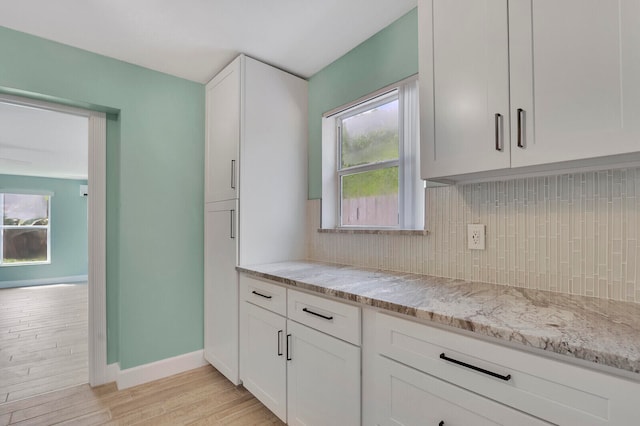 kitchen featuring light stone countertops, backsplash, light hardwood / wood-style floors, and white cabinetry