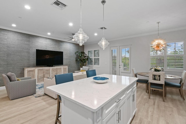 kitchen featuring a center island, white cabinetry, light wood-type flooring, decorative light fixtures, and ornamental molding