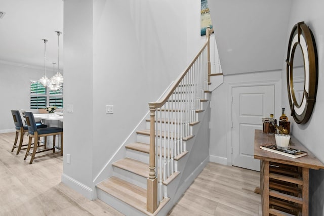 staircase with hardwood / wood-style flooring, a notable chandelier, and ornamental molding