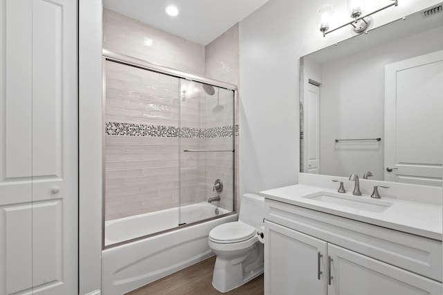 full bathroom with hardwood / wood-style floors, toilet, vanity, and shower / bath combination with glass door