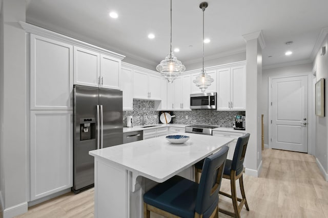 kitchen with pendant lighting, appliances with stainless steel finishes, sink, white cabinetry, and a kitchen island