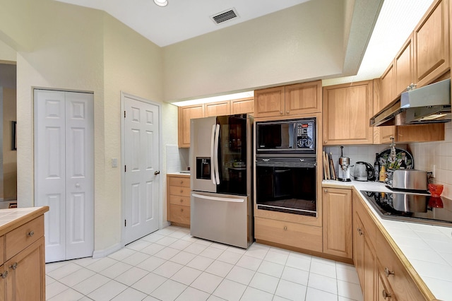 kitchen with under cabinet range hood, light tile patterned floors, black appliances, backsplash, and tile countertops
