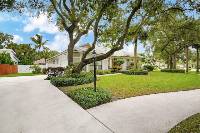view of front of house with driveway, a tile roof, fence, a front lawn, and a garage