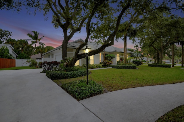 view of front of property featuring fence, concrete driveway, a tiled roof, stucco siding, and a lawn