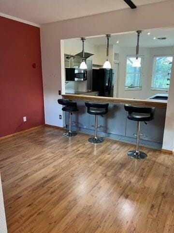 kitchen with black refrigerator, pendant lighting, hardwood / wood-style flooring, and a kitchen bar