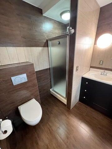 bathroom featuring tile walls, a shower with door, hardwood / wood-style floors, vanity, and toilet