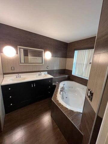 bathroom with hardwood / wood-style flooring, vanity, and a relaxing tiled tub