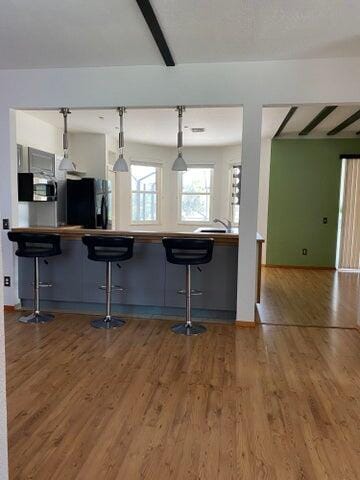 kitchen with hardwood / wood-style flooring, decorative light fixtures, beam ceiling, and a kitchen bar