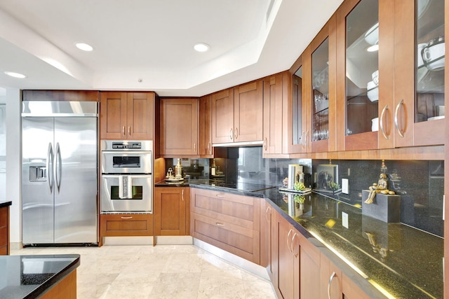 kitchen with decorative backsplash, stainless steel appliances, a tray ceiling, and dark stone countertops