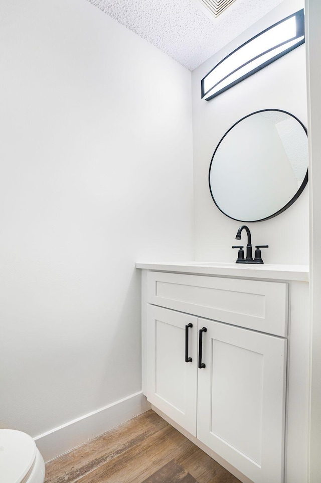 bathroom with a textured ceiling, vanity, toilet, and hardwood / wood-style flooring