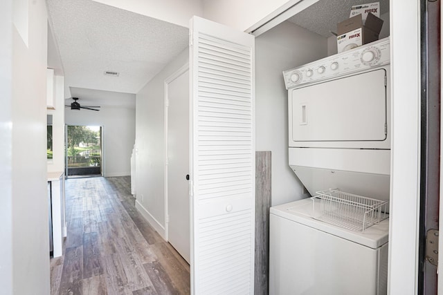 laundry room with wood-type flooring, stacked washer and dryer, ceiling fan, and a textured ceiling