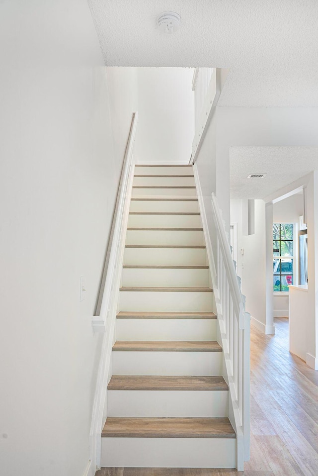 staircase with wood-type flooring and a textured ceiling