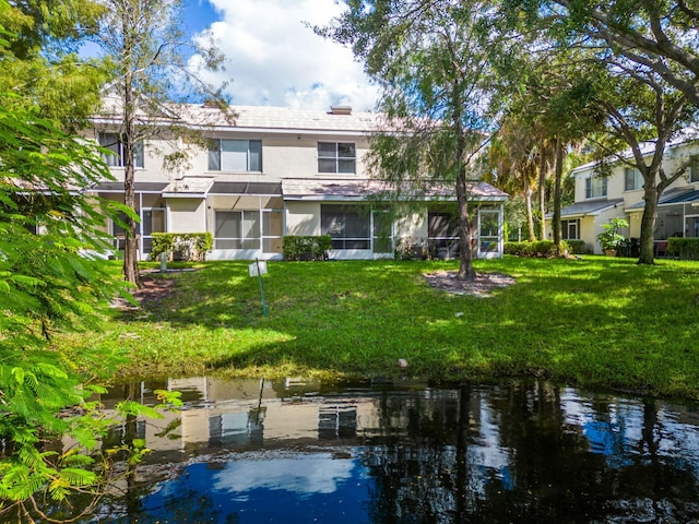 back of property with a water view, a yard, and a sunroom