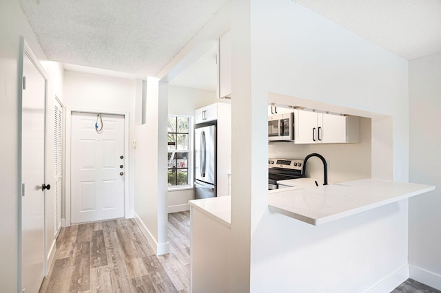 kitchen with light wood-type flooring, a textured ceiling, white cabinetry, kitchen peninsula, and appliances with stainless steel finishes